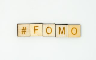 The word #FOMO (hashtag FOMO) spelled out in wooden alphabet tiles on an isolated white background. FOMO is an acronym meaning Fear of Missing out and used on social media by youths and millennials